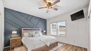 A bedroom with a bed, nightstands, a ceiling fan, a TV, and a window with blinds. - Newly Rennovated • Walking Distance to Downtown • Cripple Creek Donkies (Cripple Creek)