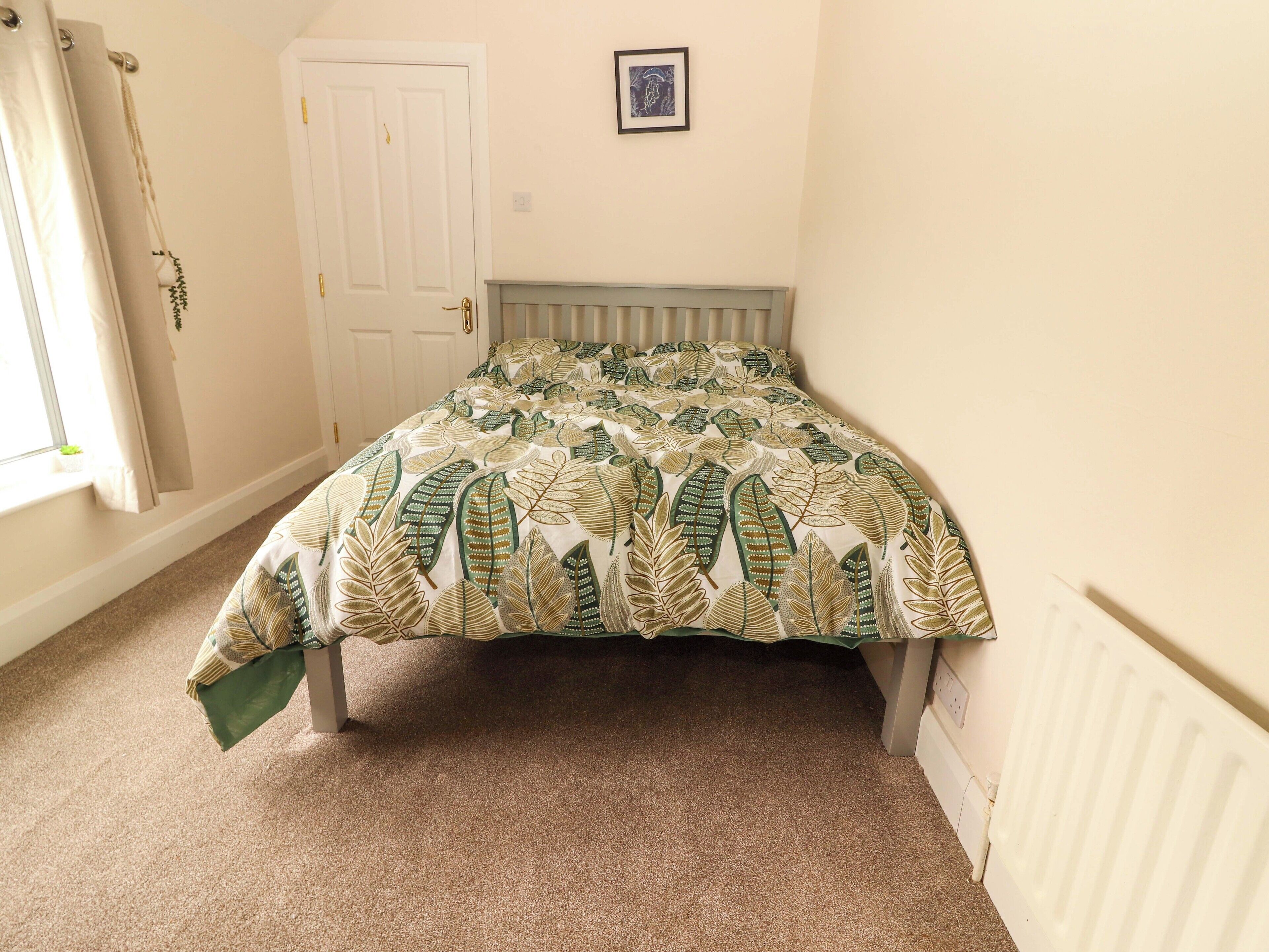 A bedroom with a bed, a door, a radiator, and a window with curtains.