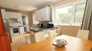 A modern kitchen with white cabinets, a wooden dining table, and a view of the garden through the window. - O'CONNELL'S&NBSP;LODGE, pet friendly in Portmagee, County Kerry (Portmagee)