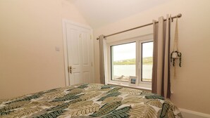 A bedroom with a bed, a window with a view of the sea, a door, and a curtain. - O'CONNELL'S&NBSP;LODGE, pet friendly in Portmagee, County Kerry (Portmagee)