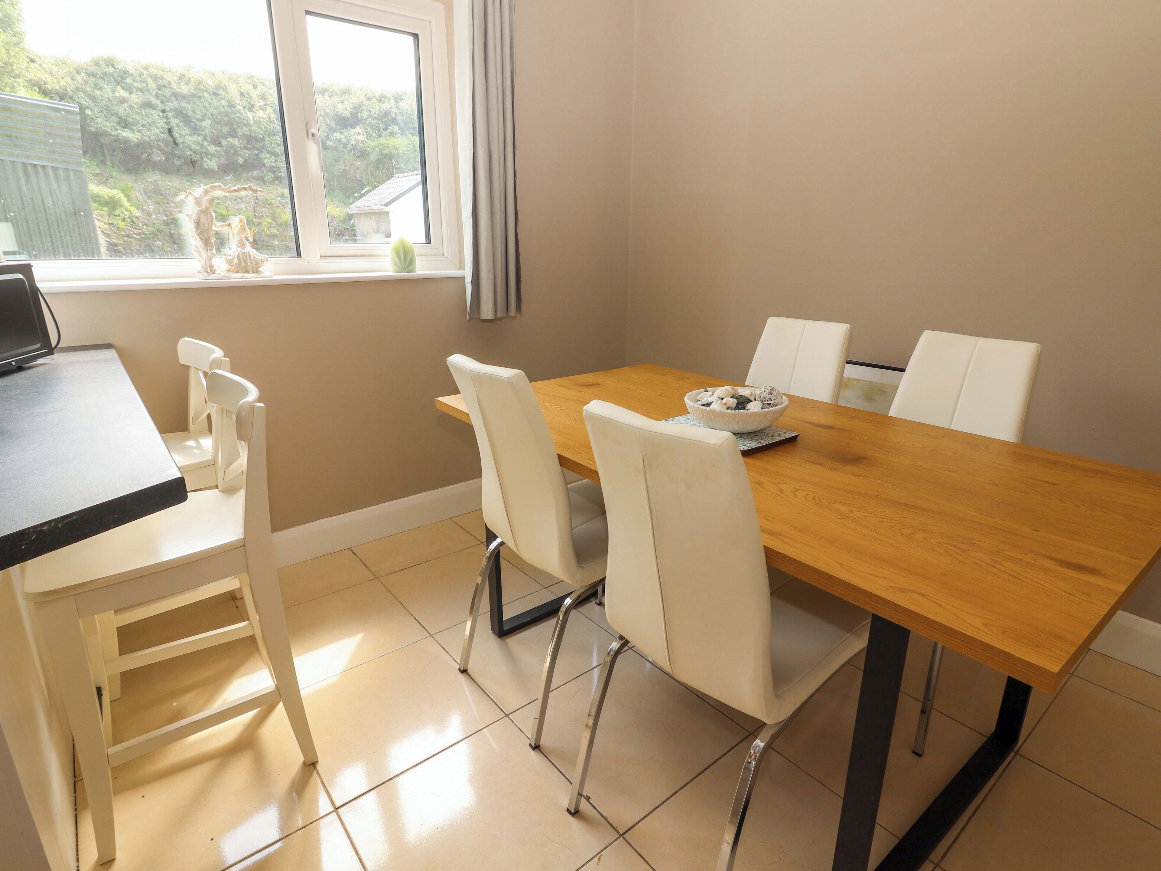 A dining area with a wooden table, white chairs, and a bowl of decorative items on the table.