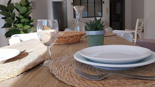 A dining table set with plates, a glass, and a fork, with a woven placemat and a potted plant. - Bright house with private pool perfect family vacation (Le Rouret)