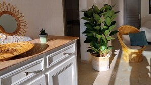 A well-lit interior with a wooden counter, a potted plant, a wicker chair, and a door in the background. - Bright house with private pool perfect family vacation (Le Rouret)