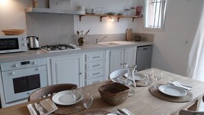 A modern kitchen with white cabinets, a gas stove, a built-in oven, and a dishwasher. There is a dining table set with plates, glasses, and cutlery. - Bright house with private pool perfect family vacation (Le Rouret)