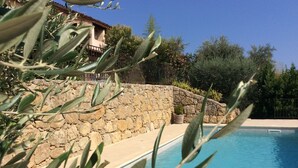 A swimming pool with a stone wall and greenery in the background. - Bright house with private pool perfect family vacation (Le Rouret)