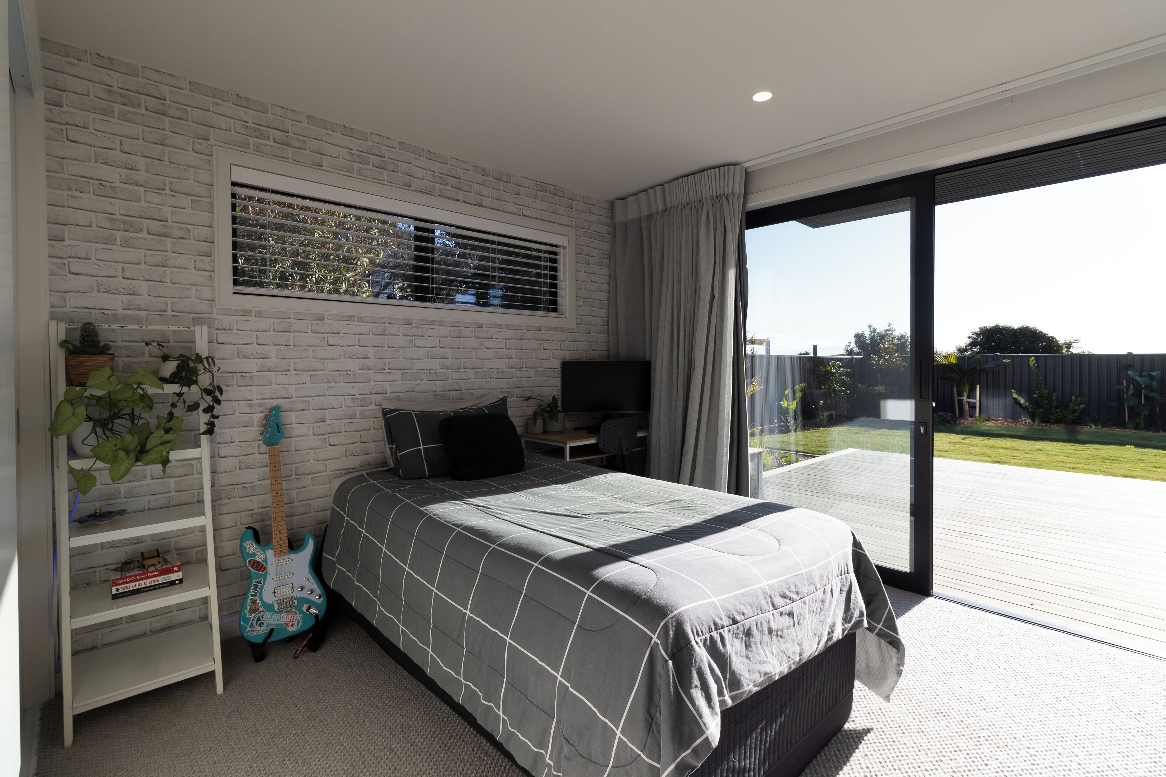 A bedroom with a bed, a TV, a guitar, and a balcony with a view of the outdoors.