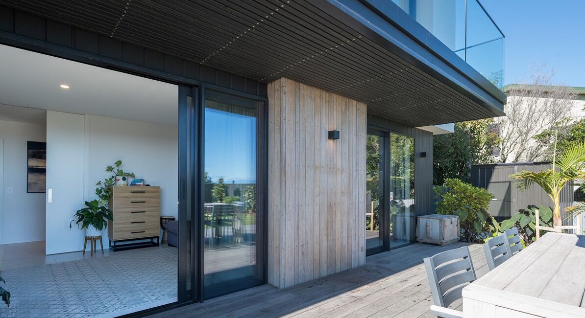 A modern house with a large sliding glass door leading to a patio area with a dining table and chairs.