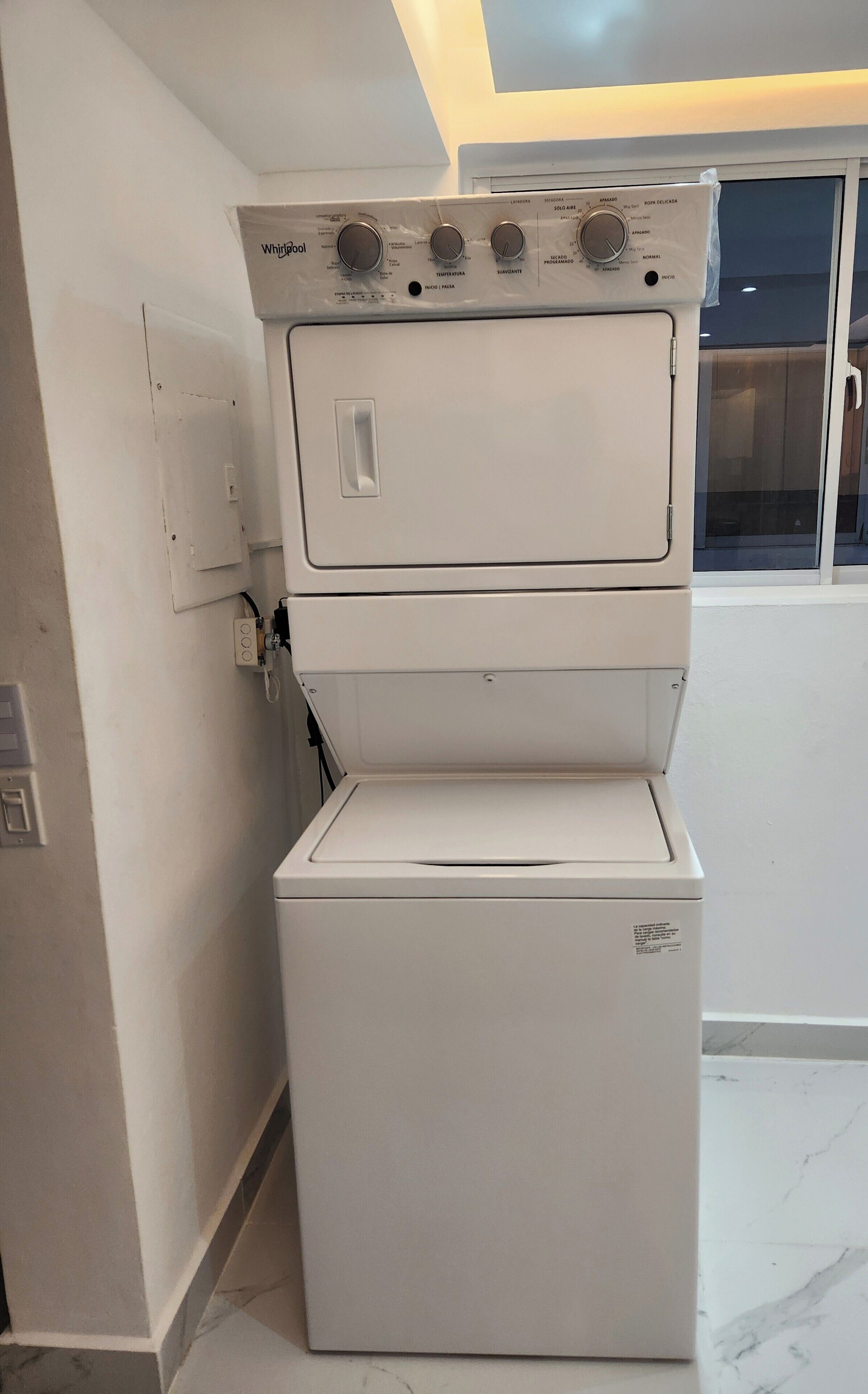 A stacked washer and dryer unit in a room with a tiled floor and a window.