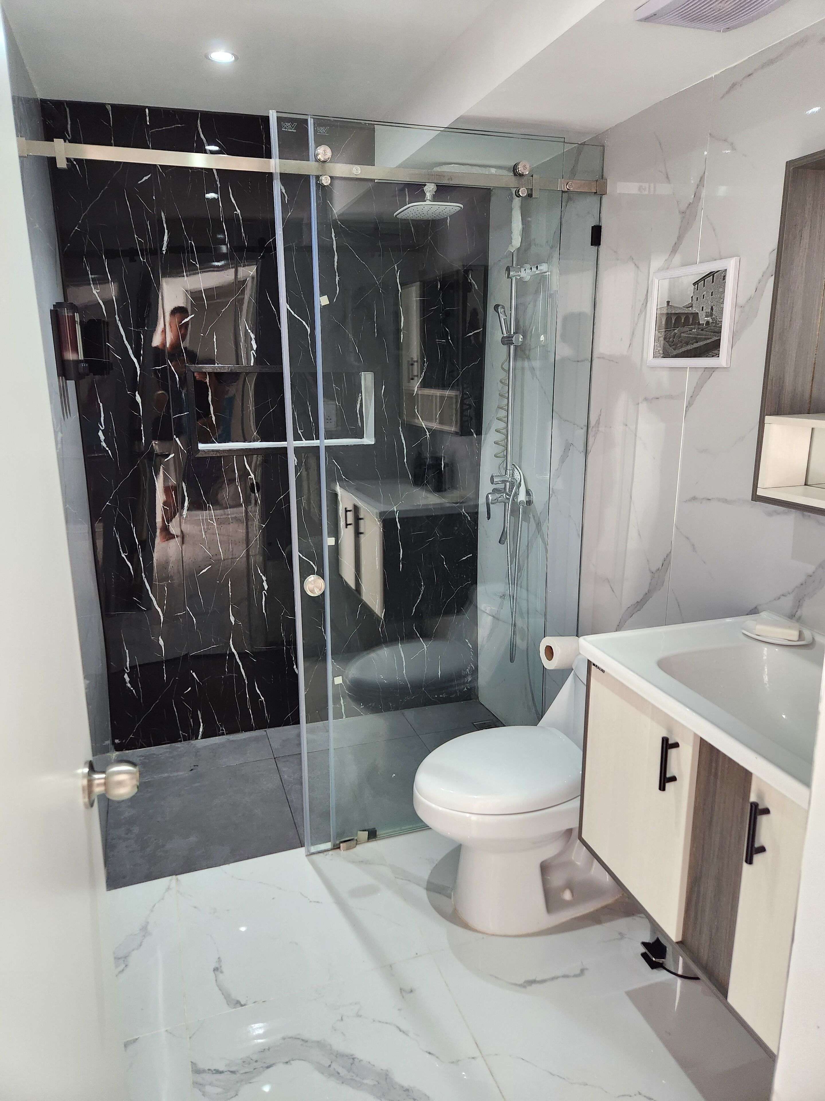 Ein modernes Badezimmer mit einer gläsernen Duschkabine, einer weißen Toilette und einem Boden aus Marmorplatten.