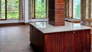 A spacious room with a large wooden column, large windows with curtains, and a wooden floor. - Mocha Chalet (Nainital)