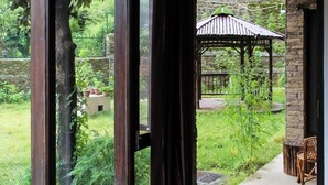 A room with large sliding glass doors leading to a garden with a gazebo and outdoor seating. - Mocha Chalet (Nainital)