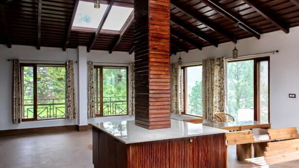A spacious room with a wooden column, large windows, and a wooden table. - Mocha Chalet (Nainital)