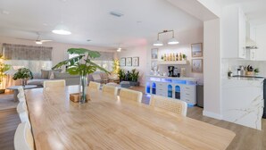 A modern living room with a wooden dining table, wicker chairs, and a large plant. - Wellness: Pool-Sauna-HotTub-ColdPlunge-Pickleball (Bradenton)