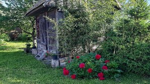 A rustic wooden structure with a sloped roof, surrounded by lush greenery and vibrant red flowers.