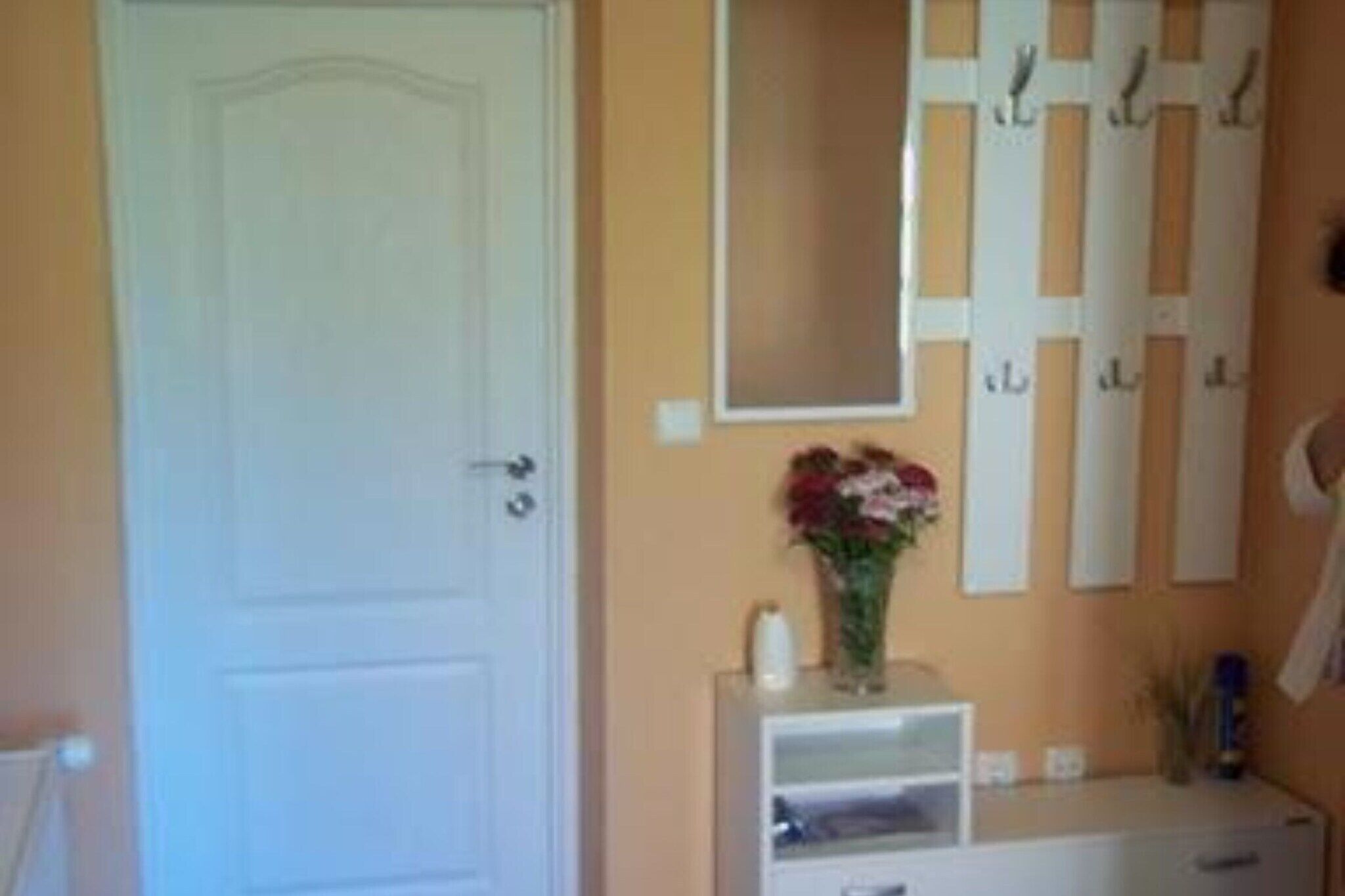 A bathroom with a white door, a mirror, a vanity with a vase of flowers, and a towel rack.