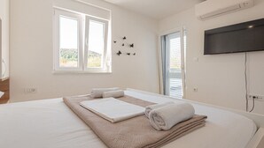 A bedroom with a bed, two windows, a wall-mounted TV, and a view of the outdoors. - Holiday Home Iva - Three Bedroom Holiday Home (Šibenik)