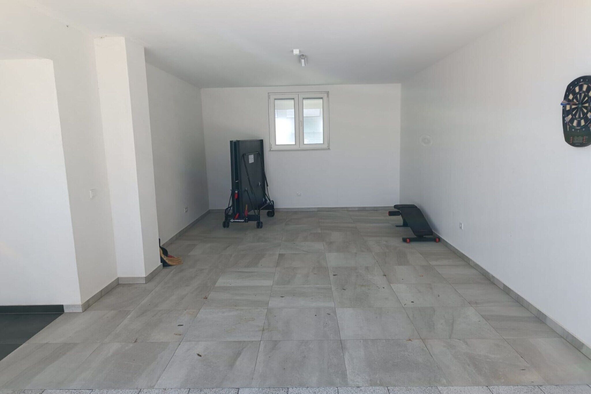 Habitació àmplia amb terra de rajola, una finestra i un joc de daus penjat a la paret.