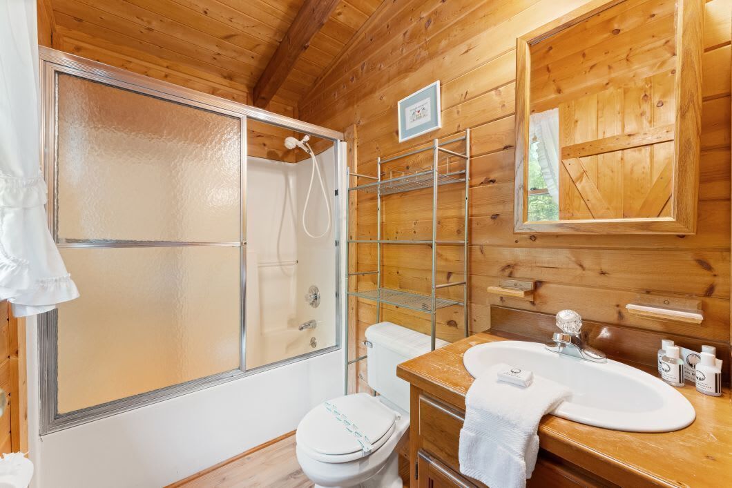 A wooden cabin bathroom with a shower, toilet, and sink.