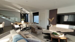 A modern living room with a sofa, armchair, dining table, and a TV. - Villa Oasis - Five Bedroom Villa with Private Pool (Trogir)