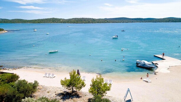 Ein Strand mit klarem türkisblauem Wasser, Booten und Liegestühlen.