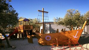Ein Spielplatz mit einer schiffartigen Spielanlage, einer Rutsche und einem Kletternetz.