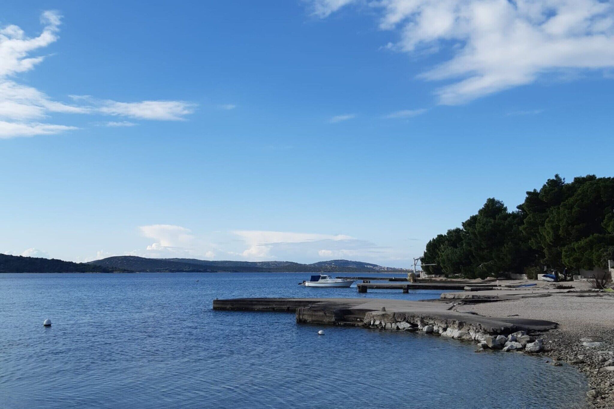 Un lac paisible où des bateaux sont amarrés à un quai, entouré d’une rive rocheuse et d’une forêt dense.
