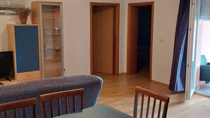 Une pièce comprenant une table à manger, des chaises, un buffet aux portes vitrées et deux portes en bois donnant sur d’autres pièces.
