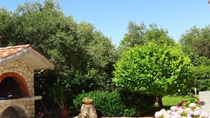 Un four extérieur en pierre, entouré d’une végétation luxuriante et de plantes en fleurs.
