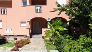 Un immeuble doté d’une entrée centrale, de plusieurs balcons et d’un jardin agrémenté de plantes et de fleurs en pot.