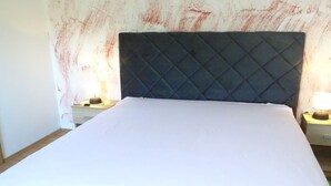 Un lit avec une tête de lit matelassée, deux tables de chevet avec des lampes et un mur sobre.