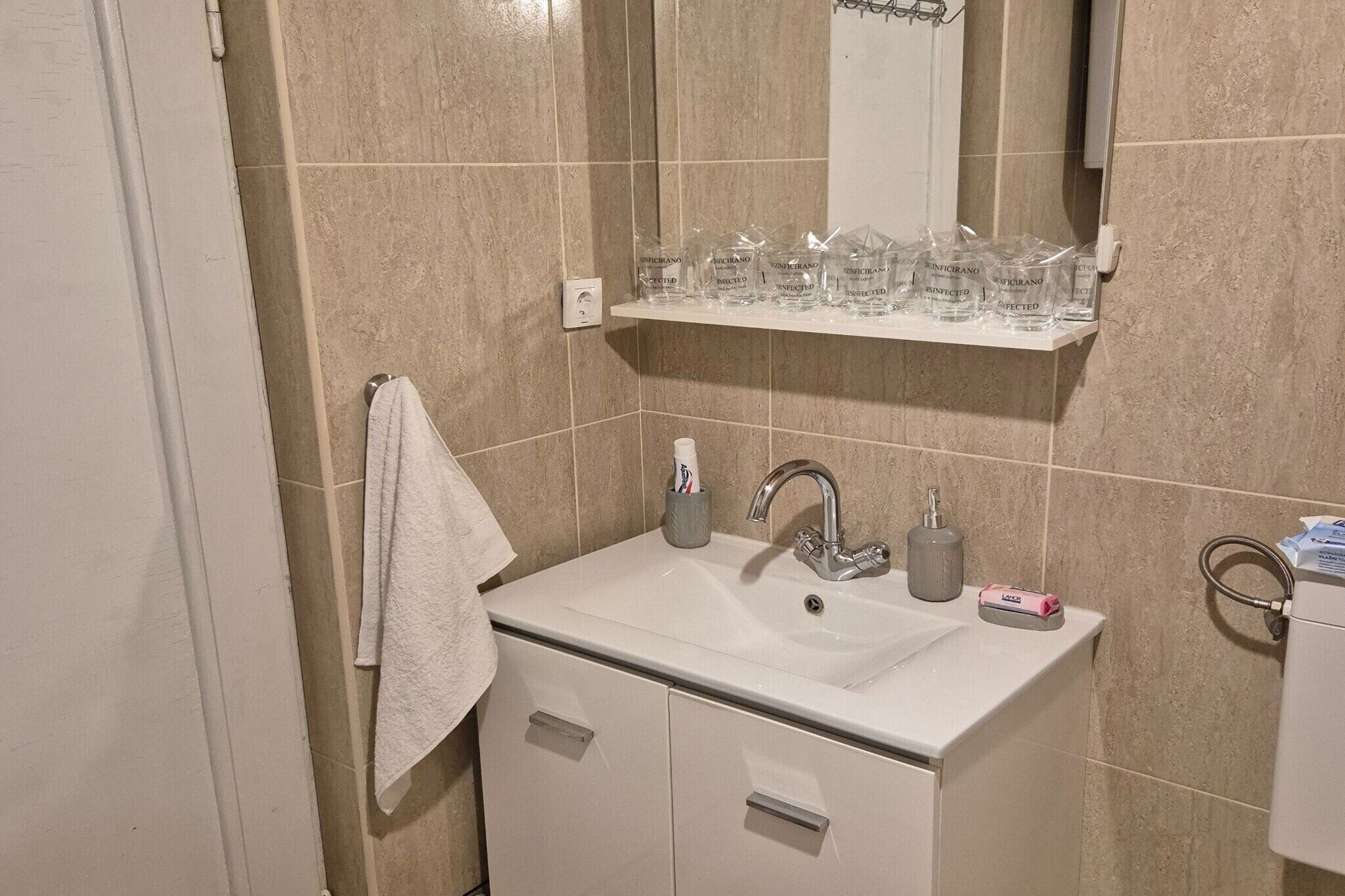 Un baño con un lavabo blanco, un espejo y un estante sobre el lavabo que contiene recipientes de vidrio.