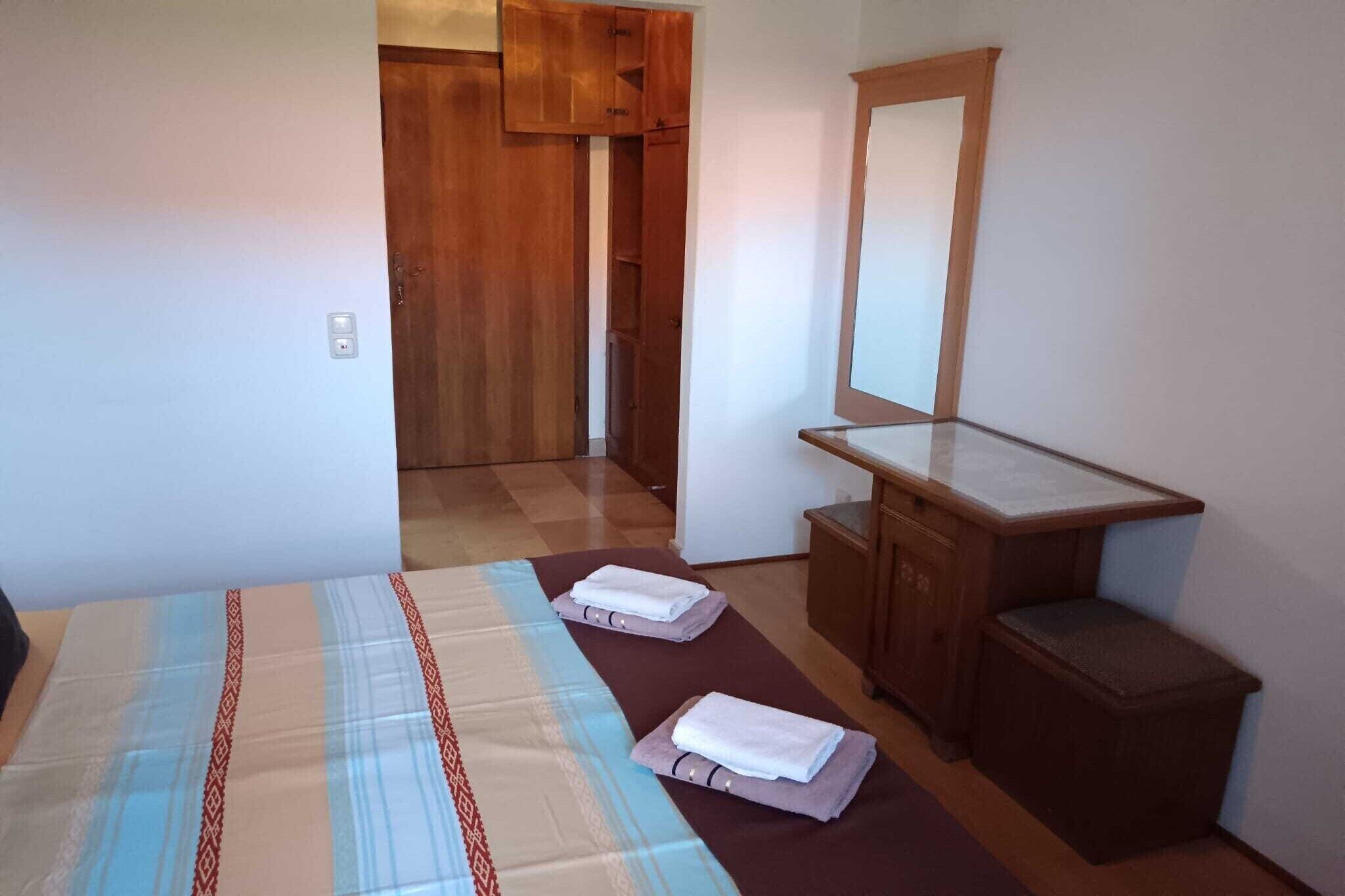 A small, clean room with a bed, a wooden desk, and a mirror.