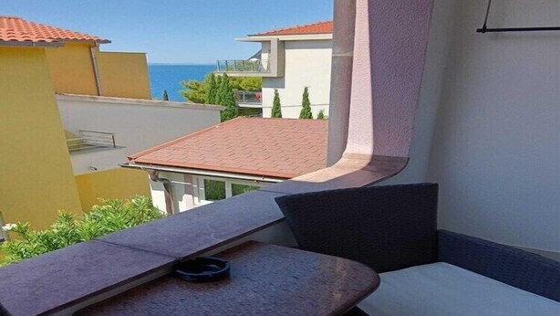 Ein Balkon mit Tisch und Stuhl, der auf einen Wohnbereich mit Häusern und Meerblick blickt.