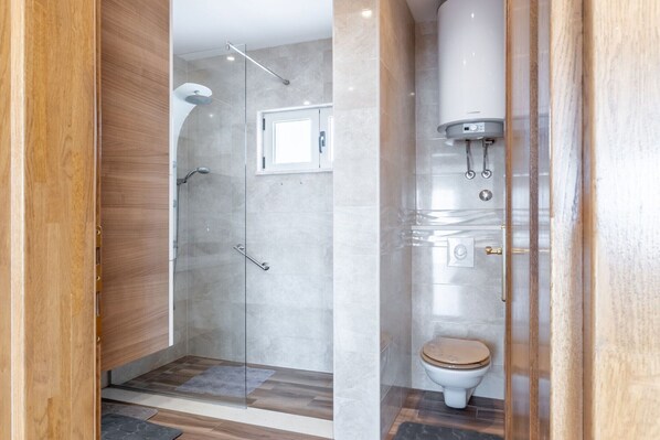 A modern bathroom with a glass-enclosed shower, a toilet, and a water heater. - Apartment Merita - Two Bedroom Apartment with Balcony (Kastel Kambelovac)