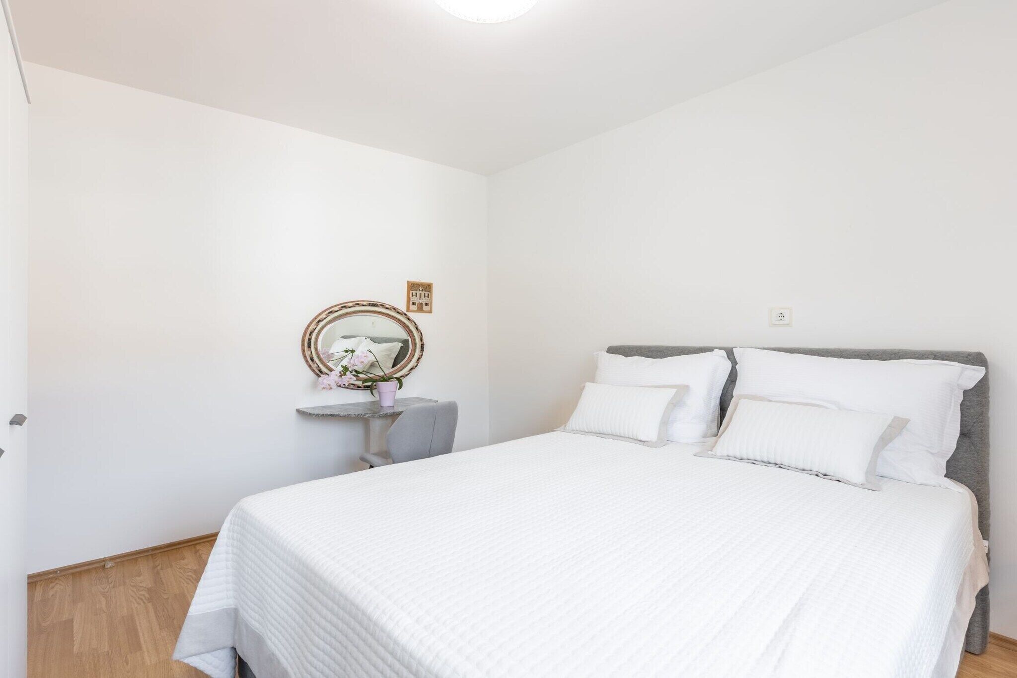 A neatly arranged bedroom with a large bed, a bedside table, a mirror, and a small desk.