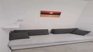 A white sofa with four grey cushions, a white side table, and a wall-mounted picture of a sunset.