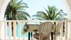 A balcony with a table and chairs, overlooking palm trees and a body of water.