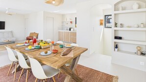 Un espace repas moderne avec une table en bois, des chaises blanches et une variété de fruits et de boissons.