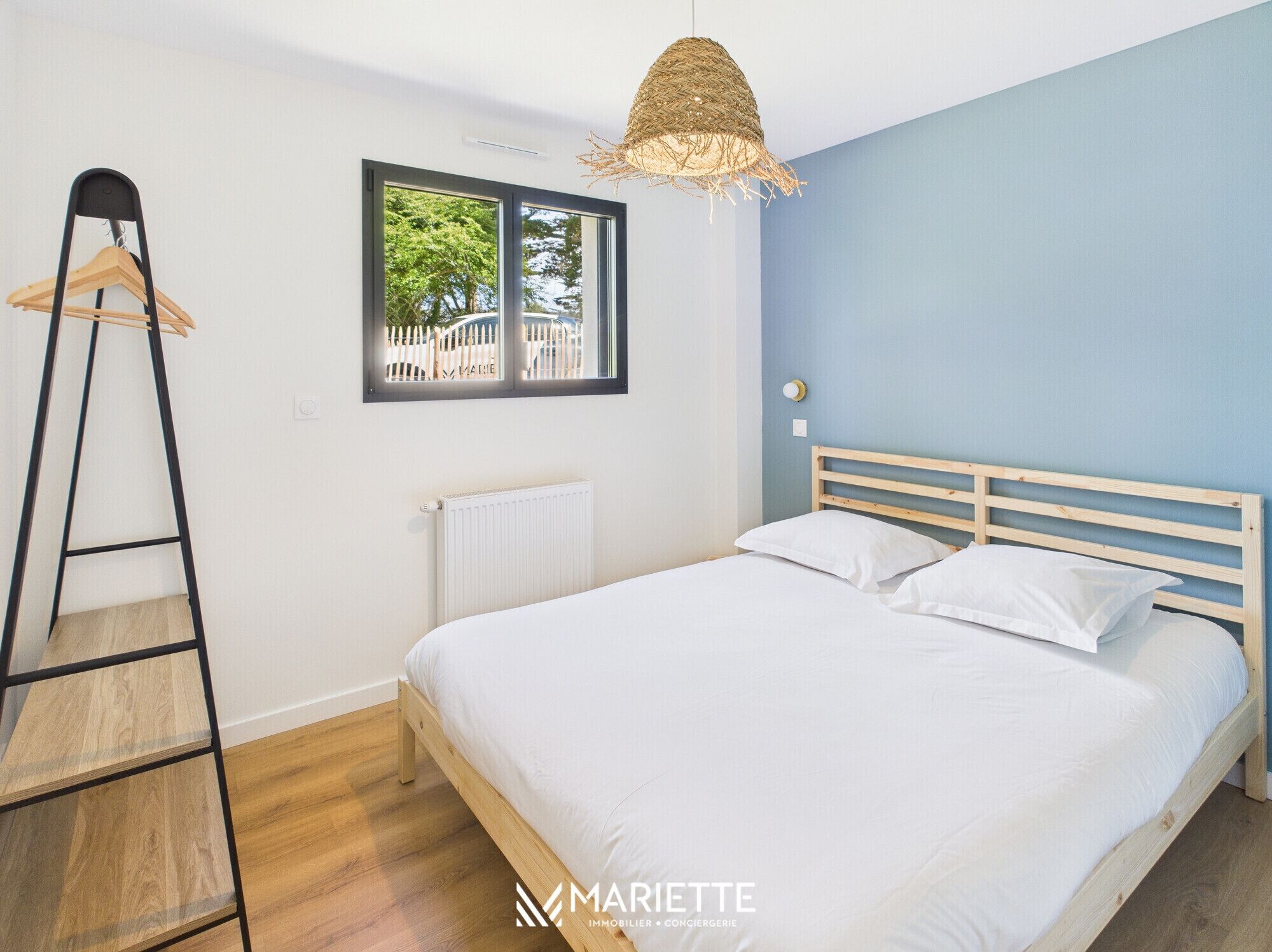 A bedroom with a bed, a wooden ladder, a window, and a hanging light fixture.