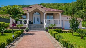 A two-story house with a red-tiled roof, a white exterior, and a front porch with steps leading to a door. - Villa Mia 2 - Six Bedroom Villa with Private Pool (Krivodol)