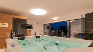 A modern spa room with a large hot tub, wooden paneling, and a view of the outdoors at night. - Villa Mia 2 - Six Bedroom Villa with Private Pool (Krivodol)