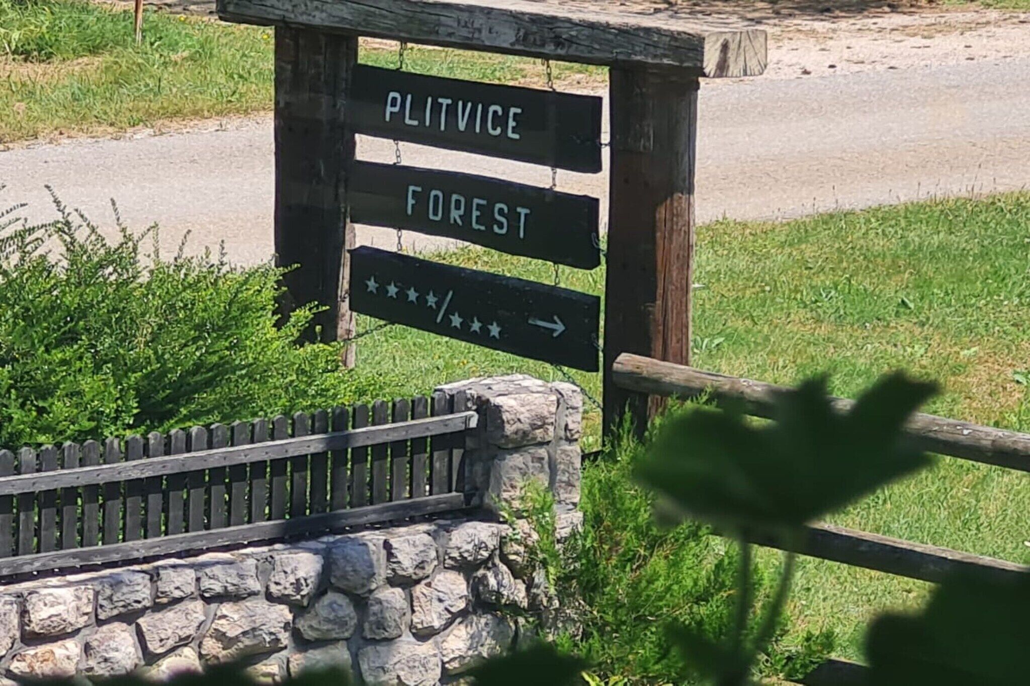 A wooden signpost with 'PLITVICE FOREST' written on it, indicating a direction to the forest area.
