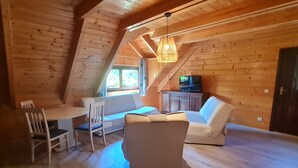 Tunnelmallinen ullakkohuone, jossa on puuseinät, ruokapöytä tuoleineen, sohva ja televisio.