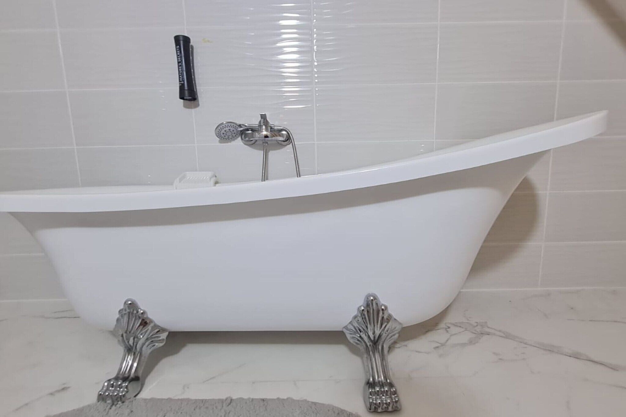 Una bañera blanca independiente con patas de garra, un cabezal de ducha y un perchero.