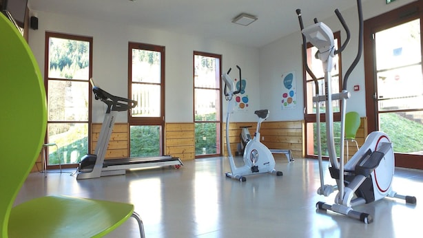 A gym with exercise equipment, large windows, and a green chair. - Apartment in Saales With Heated Pool (Saales)