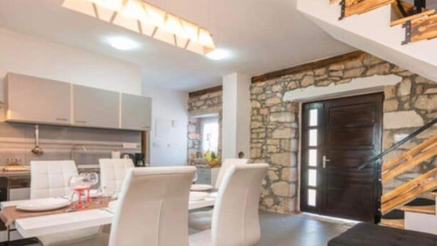 Une cuisine moderne avec des meubles blancs, un coin repas avec des chaises blanches et un mur d’accent en pierre.