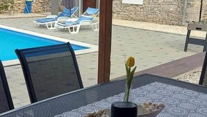 Un espace aménagé au bord de la piscine, avec des chaises longues et une table agrémentée d’un vase de fleurs.
