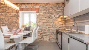 Une cuisine moderne aux murs en pierre, un coin repas avec des chaises blanches et un four encastré.