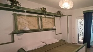 Un dormitorio con cama, mesita de noche, planta colgante y ventana con cortinas.