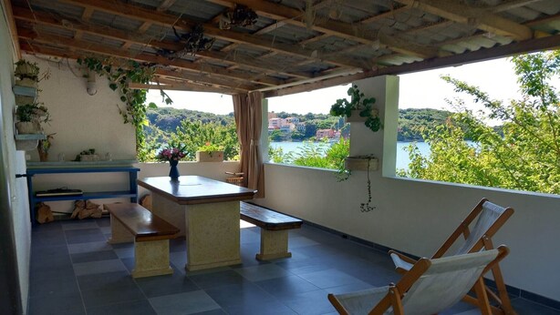 Una terraza con una mesa, bancos y vistas a un lago y colinas.